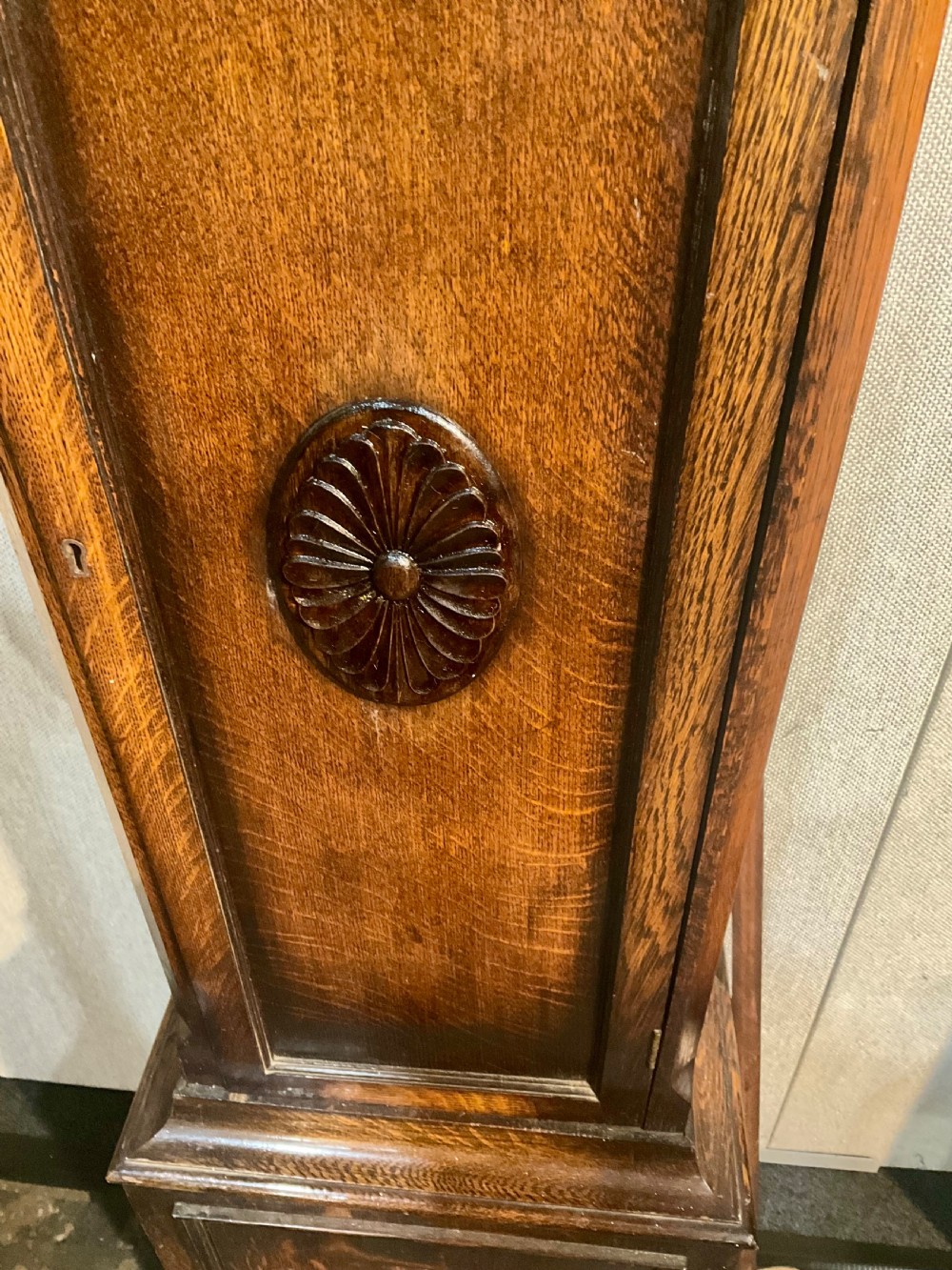 A tall dark oak grandfather clock featuring an arched hood, brass dial with spandrels, and a carved oval motif on the central door. View II