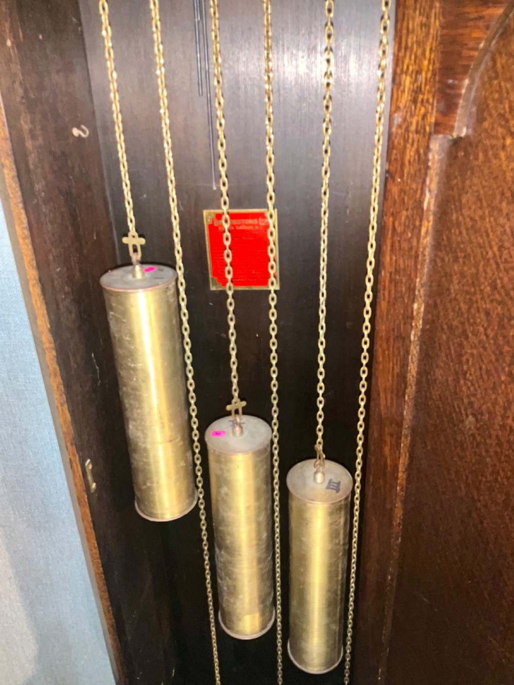 A tall dark oak grandfather clock featuring an arched hood, brass dial with spandrels, and a carved oval motif on the central door. View VIII