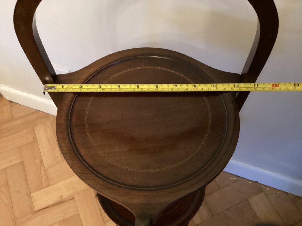 An Edwardian mahogany three-tier folding cake stand with circular trays, a carved arched handle, and tripod base. View III