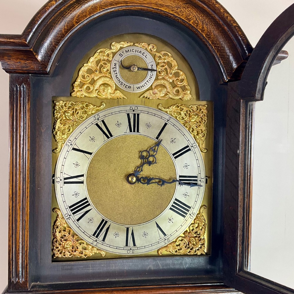 An antique dark oak longcase grandfather clock featuring an arched hood, brass dial with silvered chapter ring, and a tall panelled trunk. View III
