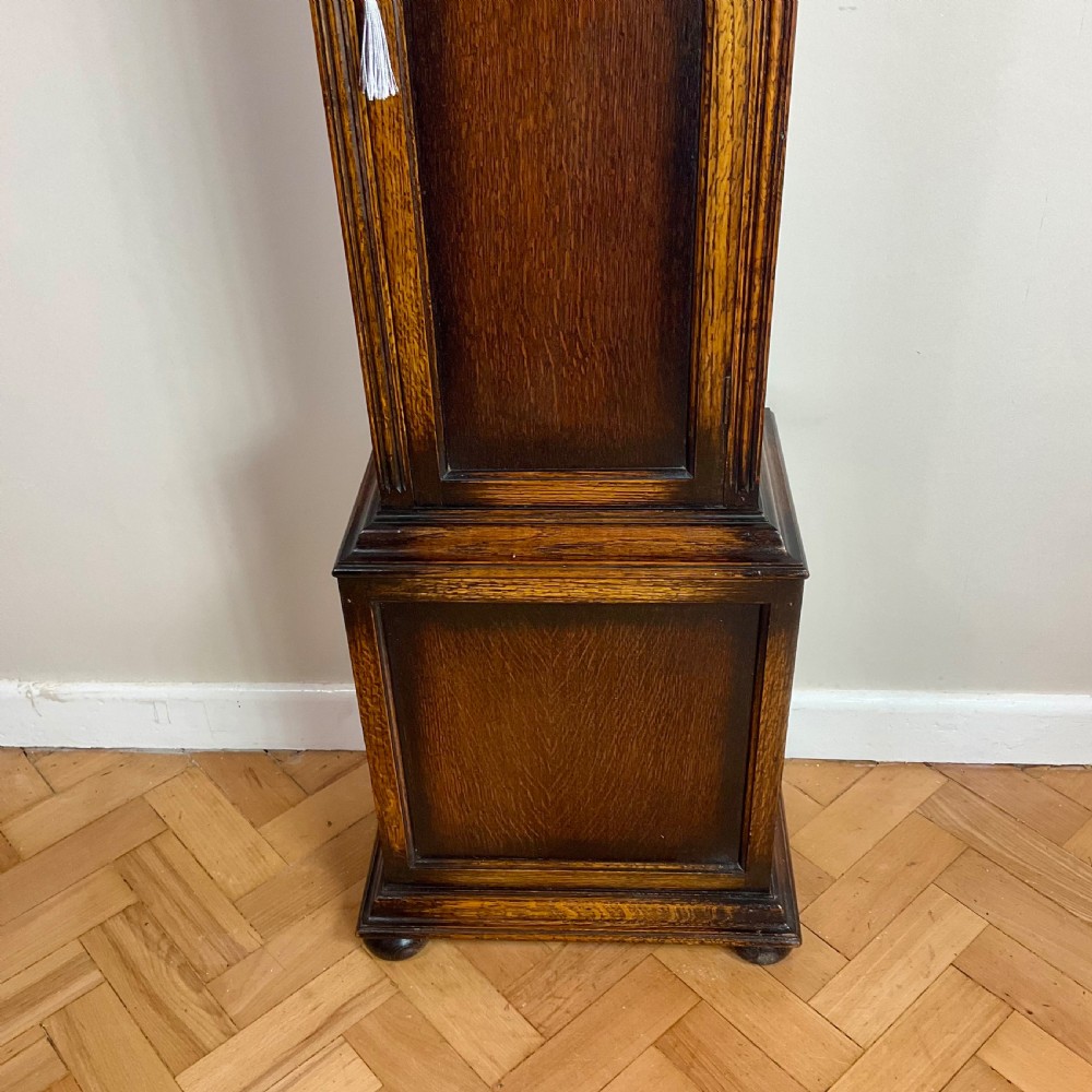 An antique dark oak longcase grandfather clock featuring an arched hood, brass dial with silvered chapter ring, and a tall panelled trunk. View VII