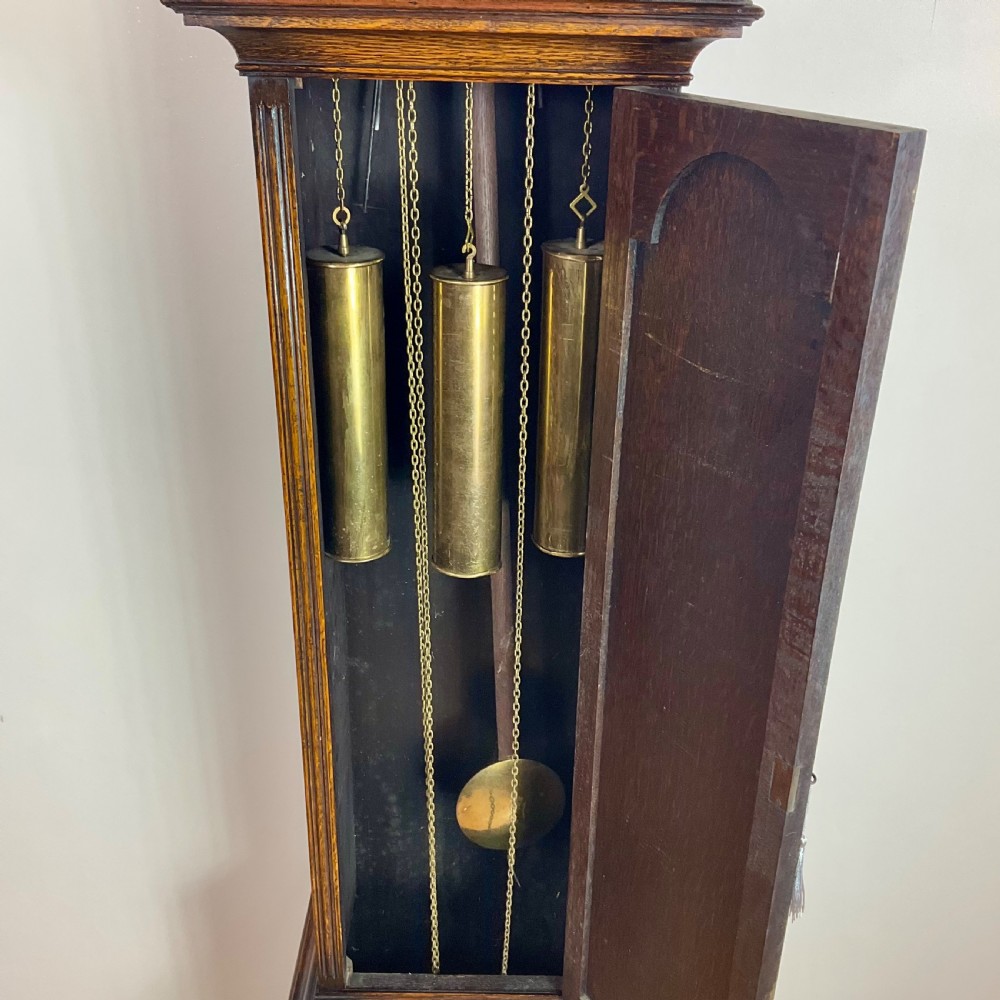An antique dark oak longcase grandfather clock featuring an arched hood, brass dial with silvered chapter ring, and a tall panelled trunk. View X