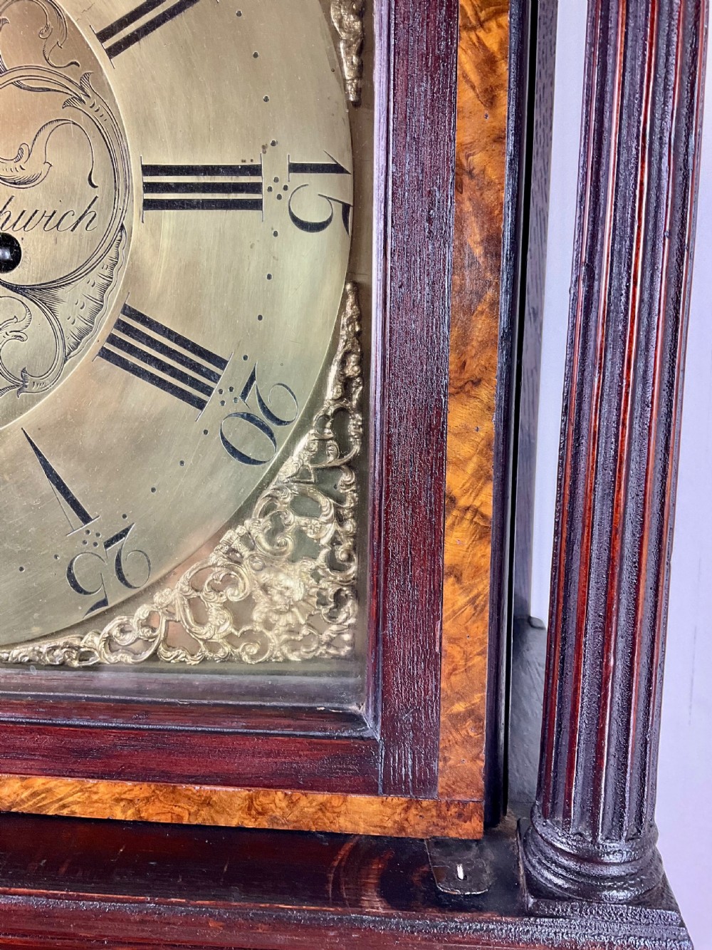 A tall Georgian dark oak longcase clock featuring an engraved brass square dial, fluted quarter-columns, and a shaped trunk door. View IV