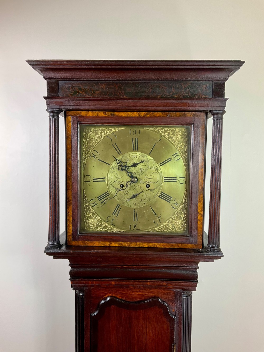A tall Georgian dark oak longcase clock featuring an engraved brass square dial, fluted quarter-columns, and a shaped trunk door. View VII