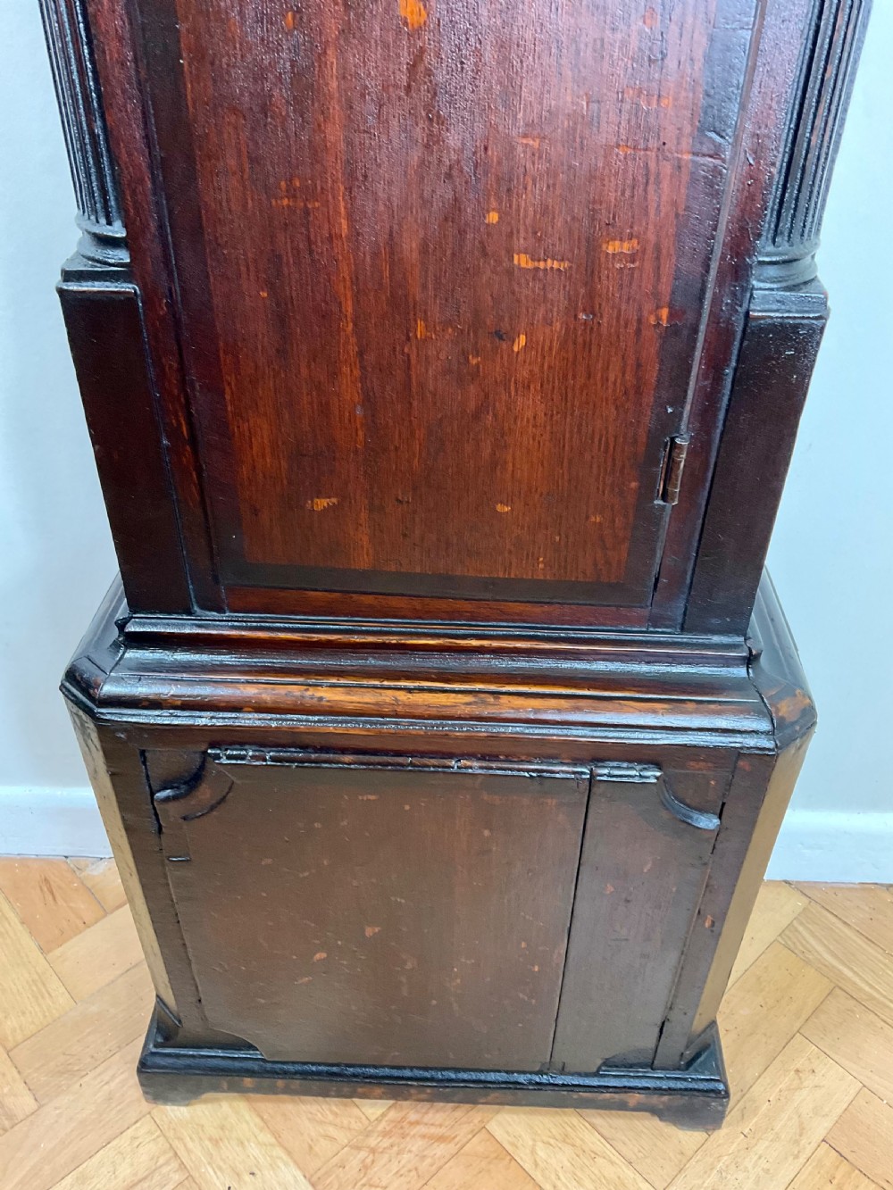 A tall Georgian dark oak longcase clock featuring an engraved brass square dial, fluted quarter-columns, and a shaped trunk door. View VIII
