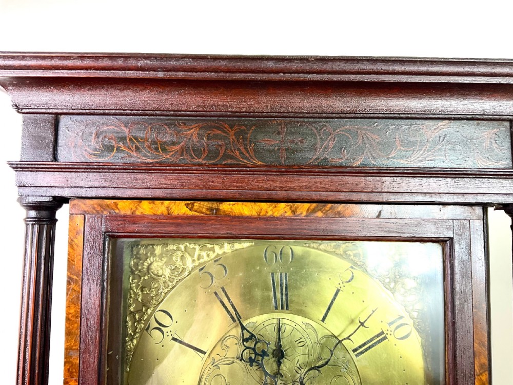 A tall Georgian dark oak longcase clock featuring an engraved brass square dial, fluted quarter-columns, and a shaped trunk door. View X