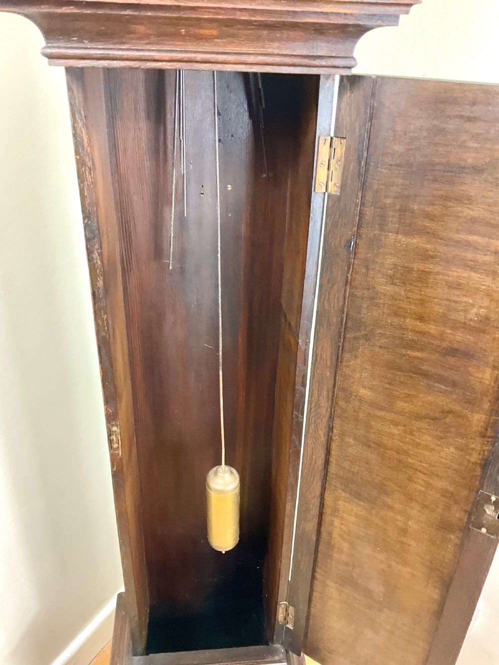 A small dark oak grandmother longcase clock featuring an arched hood, a brass dial with Roman numerals, and a carved floral motif on the trunk door. View X