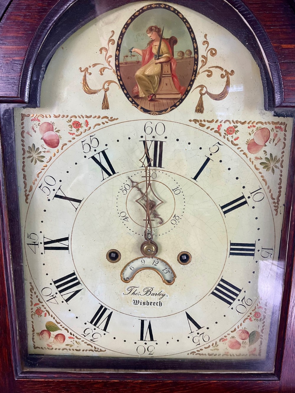 A dark oak Georgian longcase clock featuring a painted arched dial with Roman numerals and three brass urn finials on the bonnet. View II