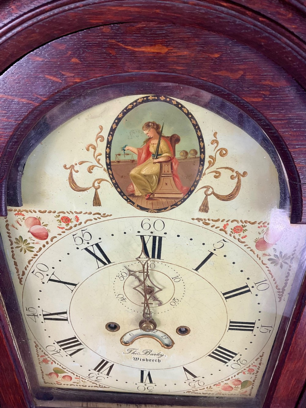 A dark oak Georgian longcase clock featuring a painted arched dial with Roman numerals and three brass urn finials on the bonnet. View IV