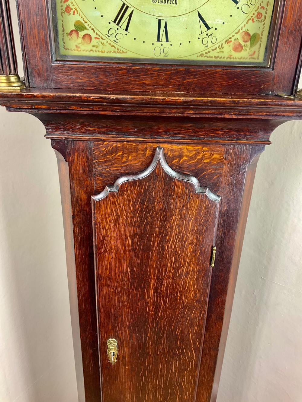 A dark oak Georgian longcase clock featuring a painted arched dial with Roman numerals and three brass urn finials on the bonnet. View VII
