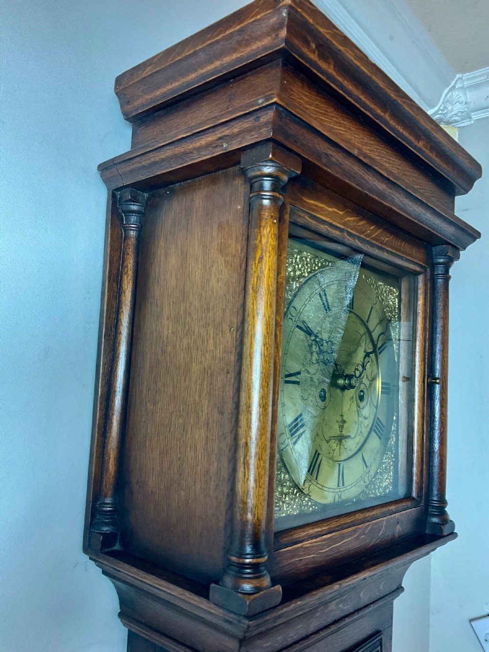 An Early Georgian oak longcase clock featuring a square brass dial with spandrels, flanked by turned columns, and a tall wooden trunk set on bracket feet. View IV