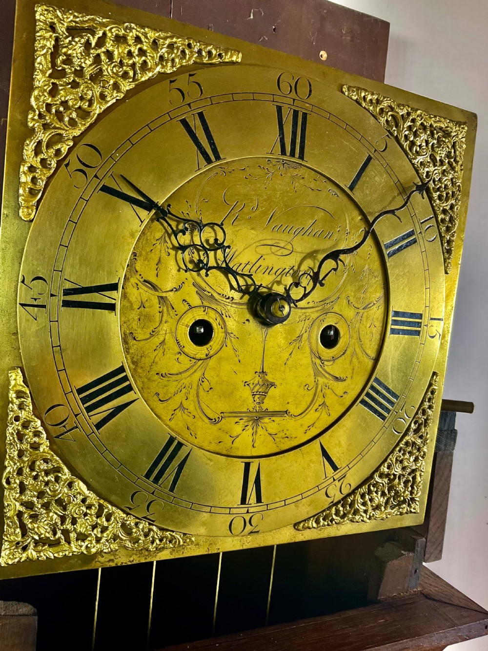 An Early Georgian oak longcase clock featuring a square brass dial with spandrels, flanked by turned columns, and a tall wooden trunk set on bracket feet. View VIII