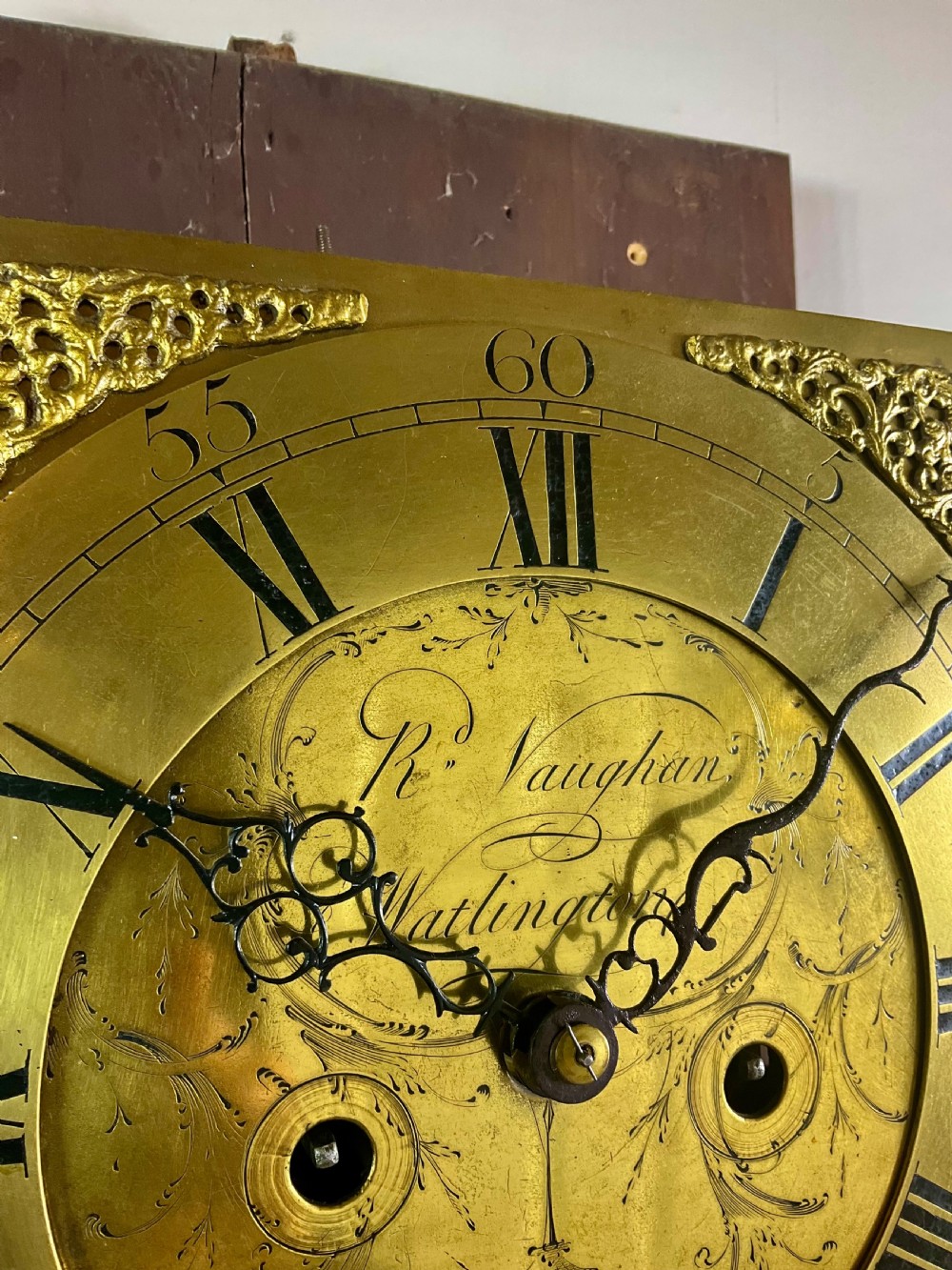 An Early Georgian oak longcase clock featuring a square brass dial with spandrels, flanked by turned columns, and a tall wooden trunk set on bracket feet. View IX