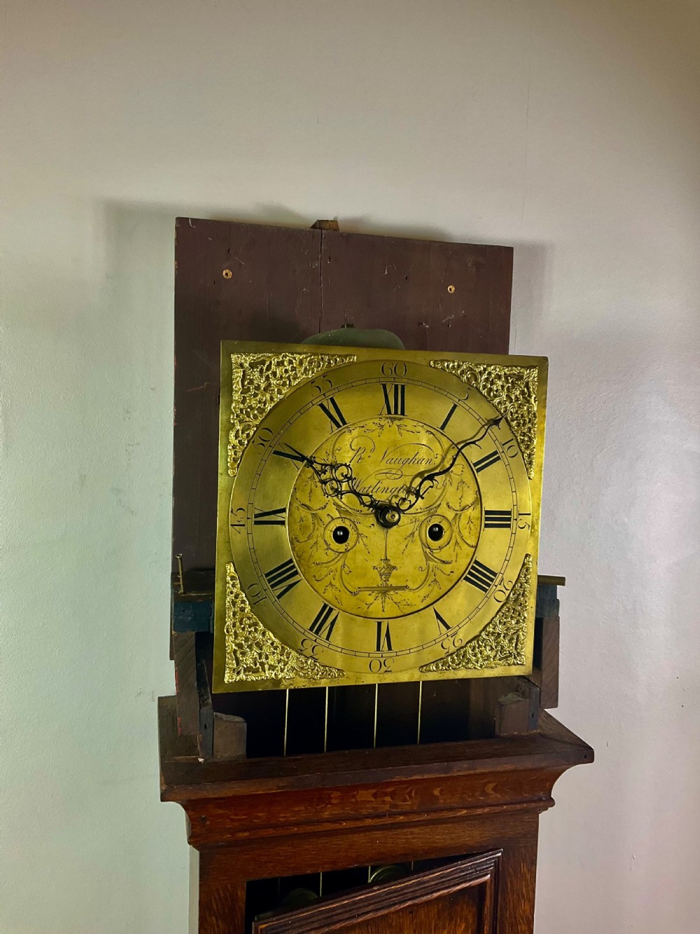 An Early Georgian oak longcase clock featuring a square brass dial with spandrels, flanked by turned columns, and a tall wooden trunk set on bracket feet. View XII