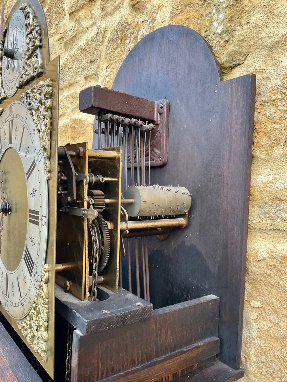 A dark oak longcase clock featuring an arched hood, silvered chapter ring dial, brass spandrels, and geometric inlaid trunk door. View X