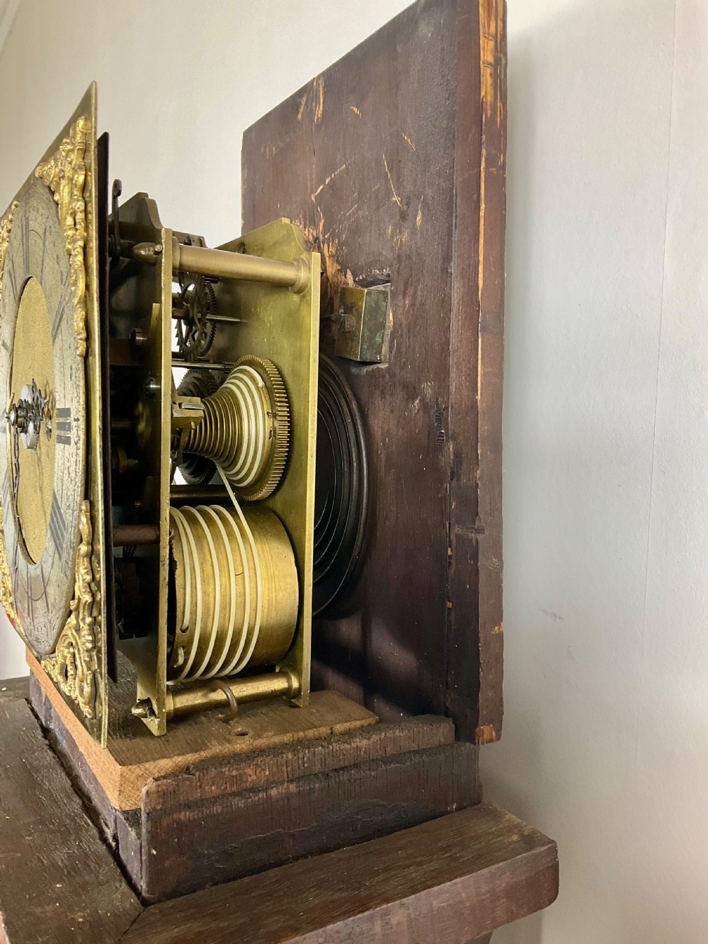 A slim Georgian oak longcase clock featuring a square brass dial with spandrels, fluted hood columns, a hinged trunk door, and a plinth base. View II