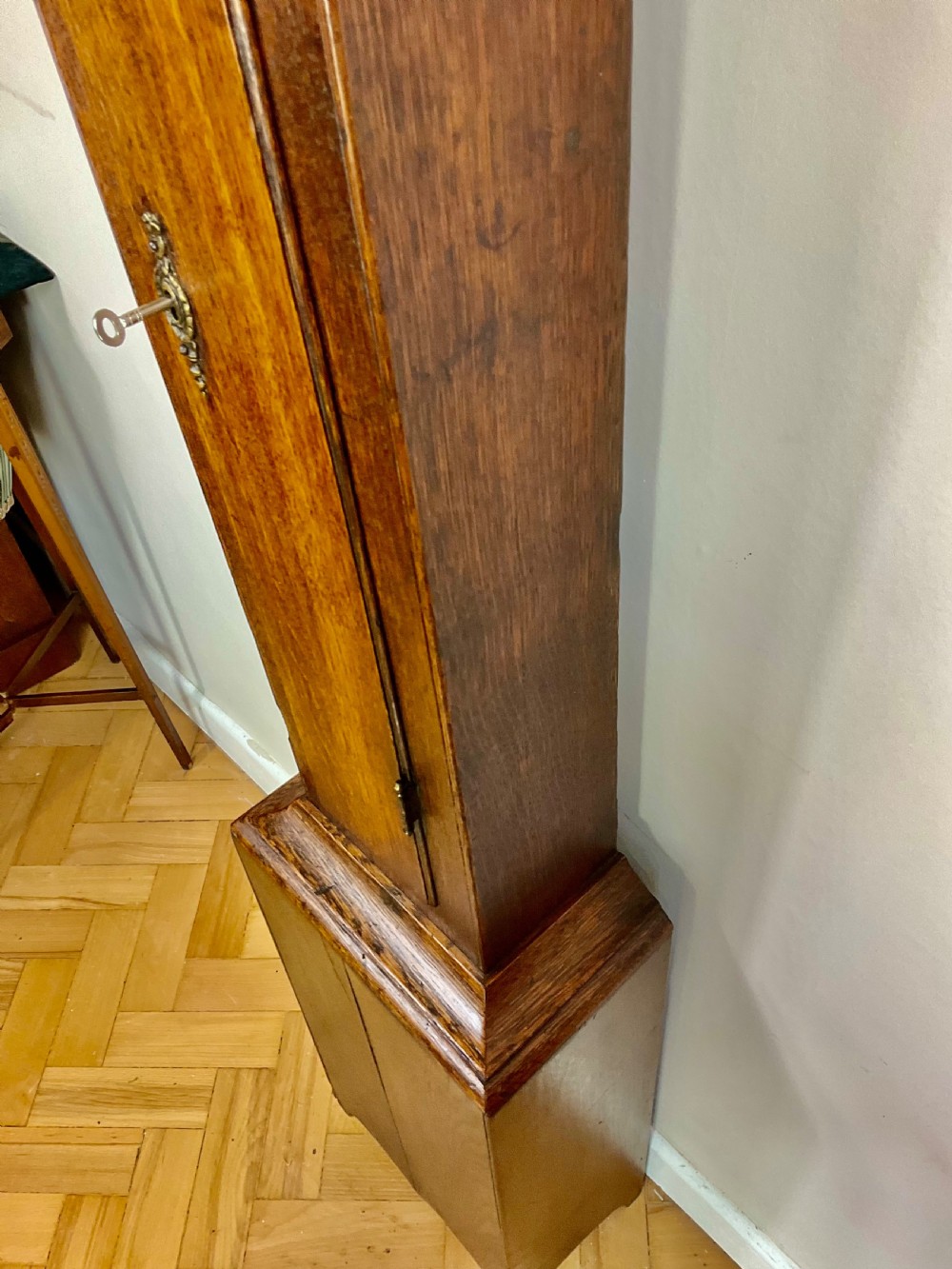 A slim Georgian oak longcase clock featuring a square brass dial with spandrels, fluted hood columns, a hinged trunk door, and a plinth base. View IV