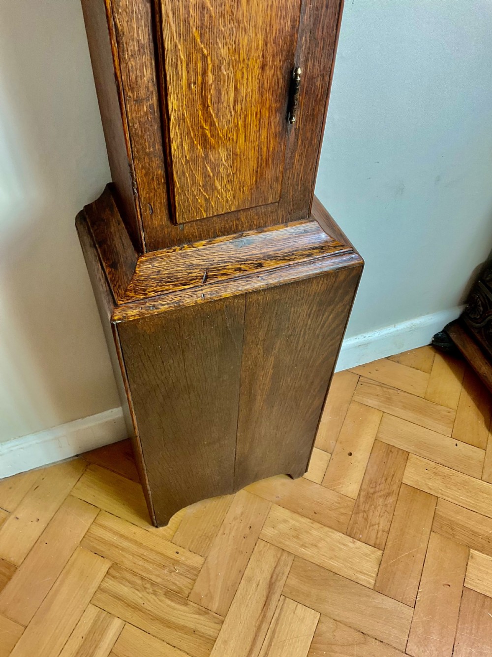 A slim Georgian oak longcase clock featuring a square brass dial with spandrels, fluted hood columns, a hinged trunk door, and a plinth base. View VI