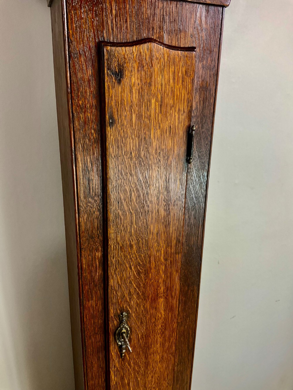 A slim Georgian oak longcase clock featuring a square brass dial with spandrels, fluted hood columns, a hinged trunk door, and a plinth base. View VII