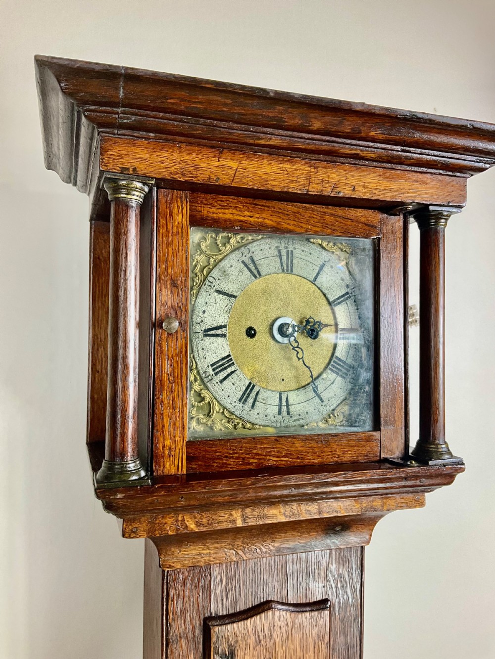 A slim Georgian oak longcase clock featuring a square brass dial with spandrels, fluted hood columns, a hinged trunk door, and a plinth base. View XI