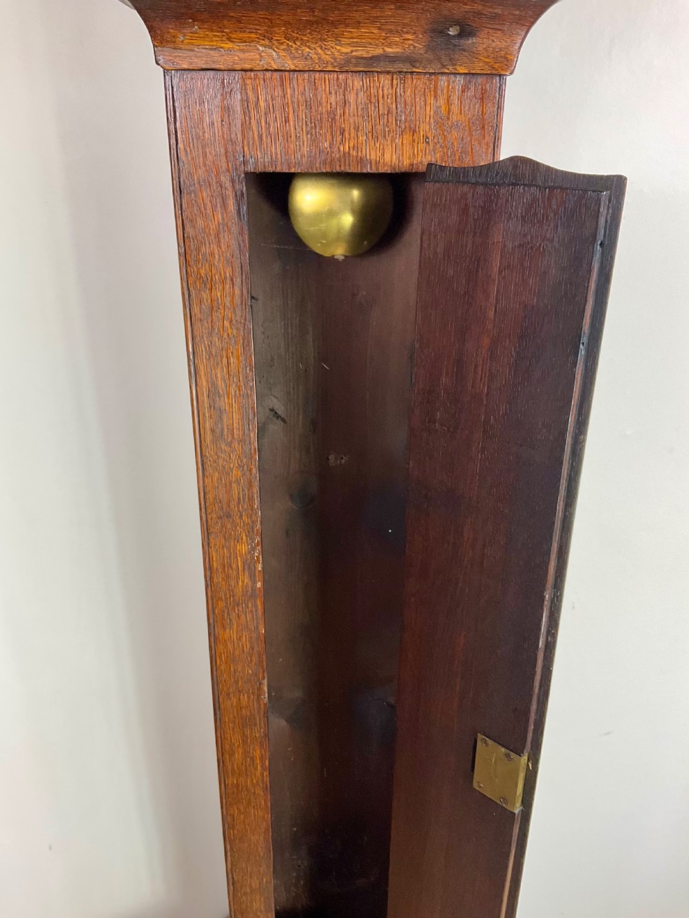 A slim Georgian oak longcase clock featuring a square brass dial with spandrels, fluted hood columns, a hinged trunk door, and a plinth base. View XII
