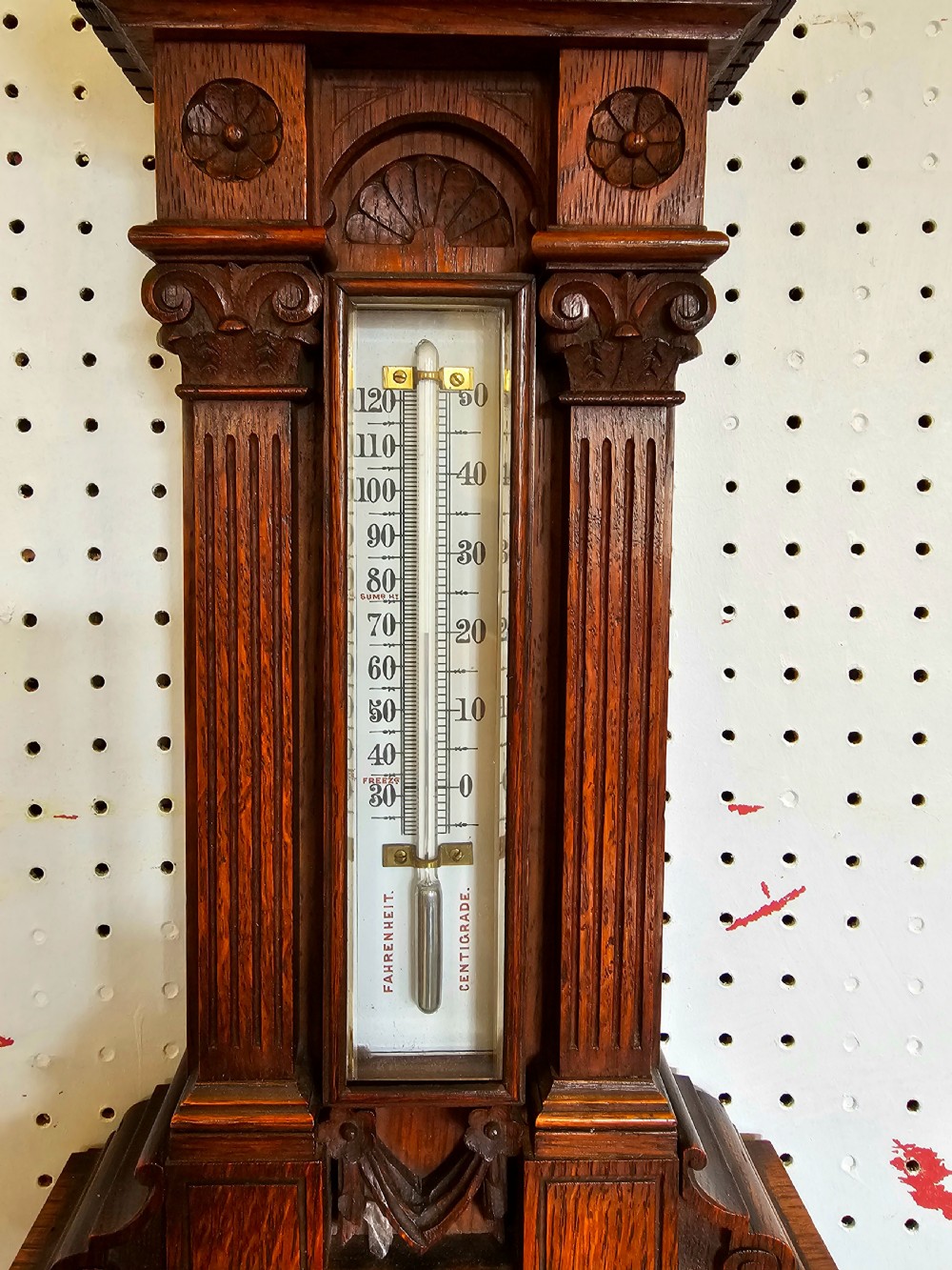 A carved oak Victorian wall barometer with an upper glass thermometer and a lower circular aneroid dial. View IV