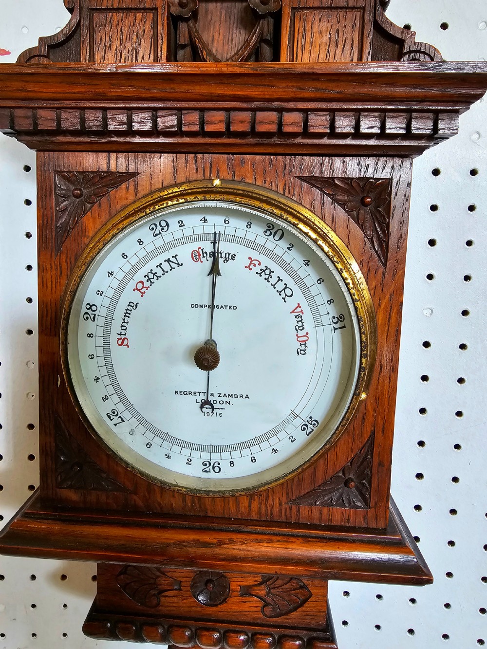 A carved oak Victorian wall barometer with an upper glass thermometer and a lower circular aneroid dial. View V