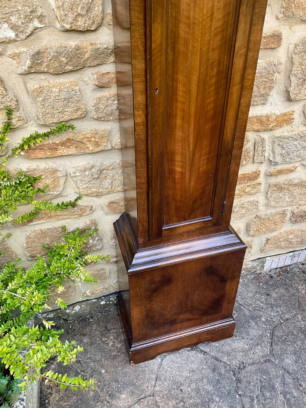 A floor-standing walnut grandmother longcase clock featuring an arched hood, brass dial with Roman numerals, long trunk door, and stepped plinth base. View III