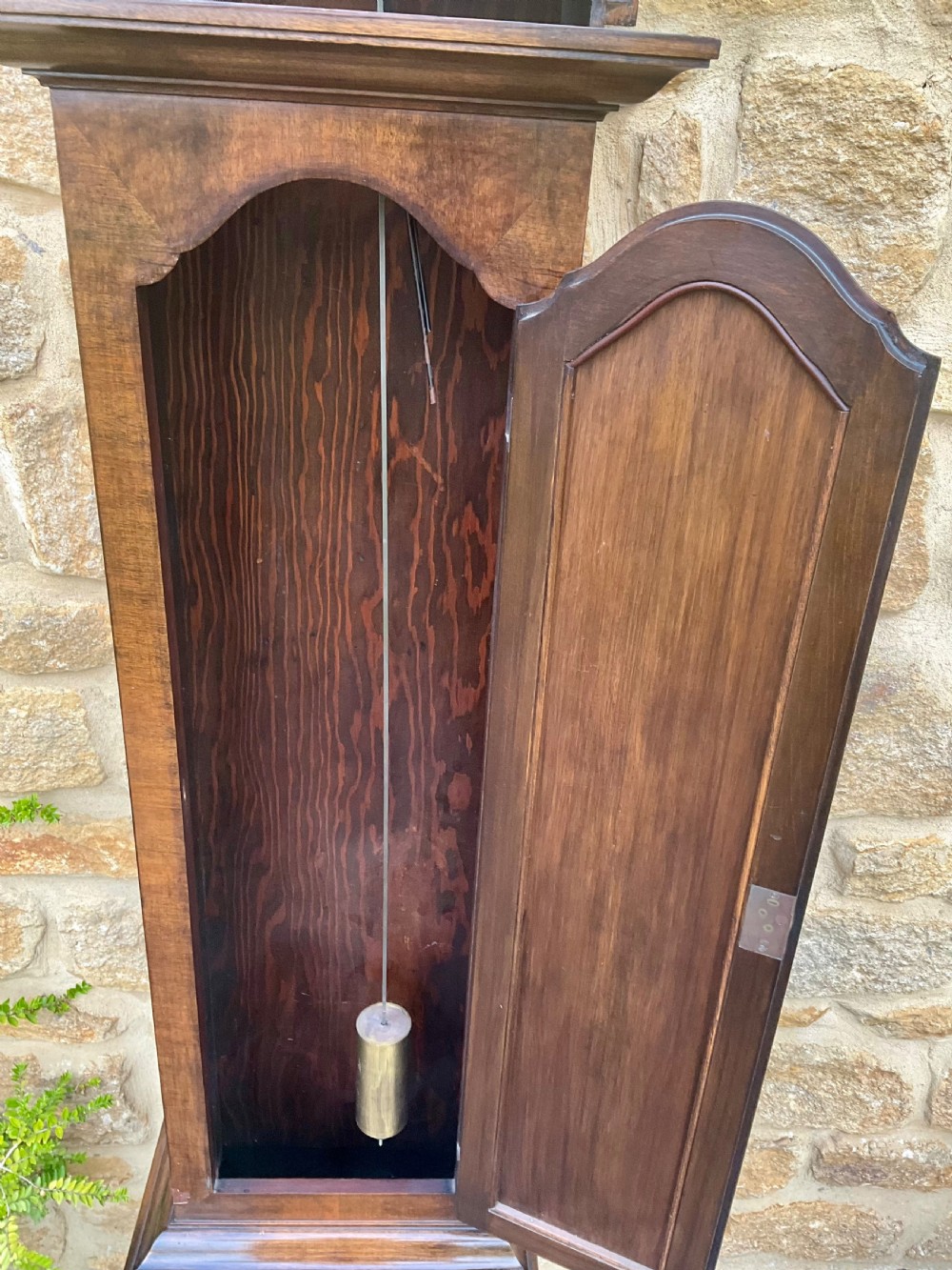 A floor-standing walnut grandmother longcase clock featuring an arched hood, brass dial with Roman numerals, long trunk door, and stepped plinth base. View IX