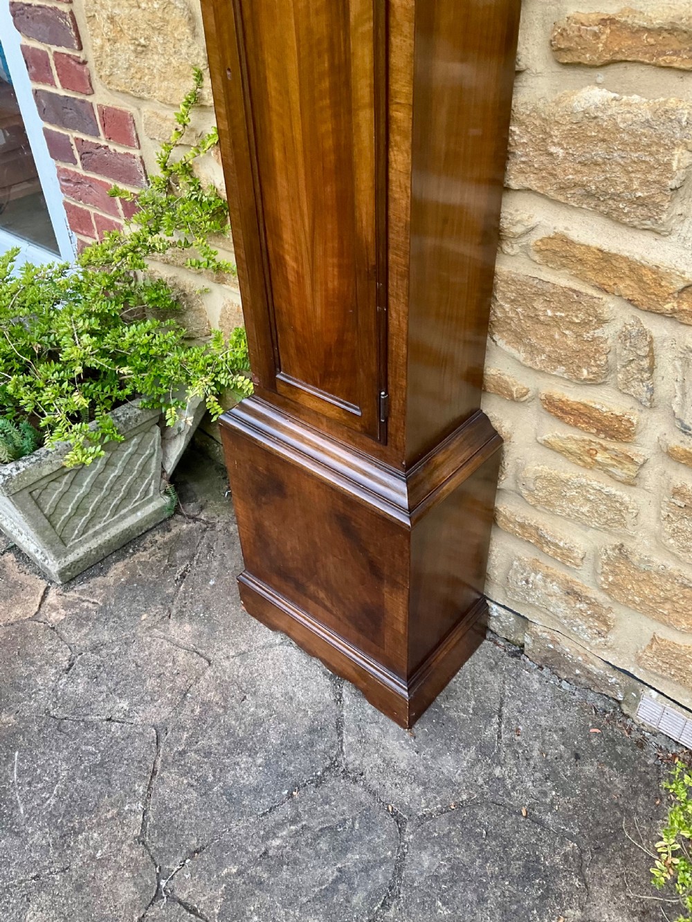 A floor-standing walnut grandmother longcase clock featuring an arched hood, brass dial with Roman numerals, long trunk door, and stepped plinth base. View XIV