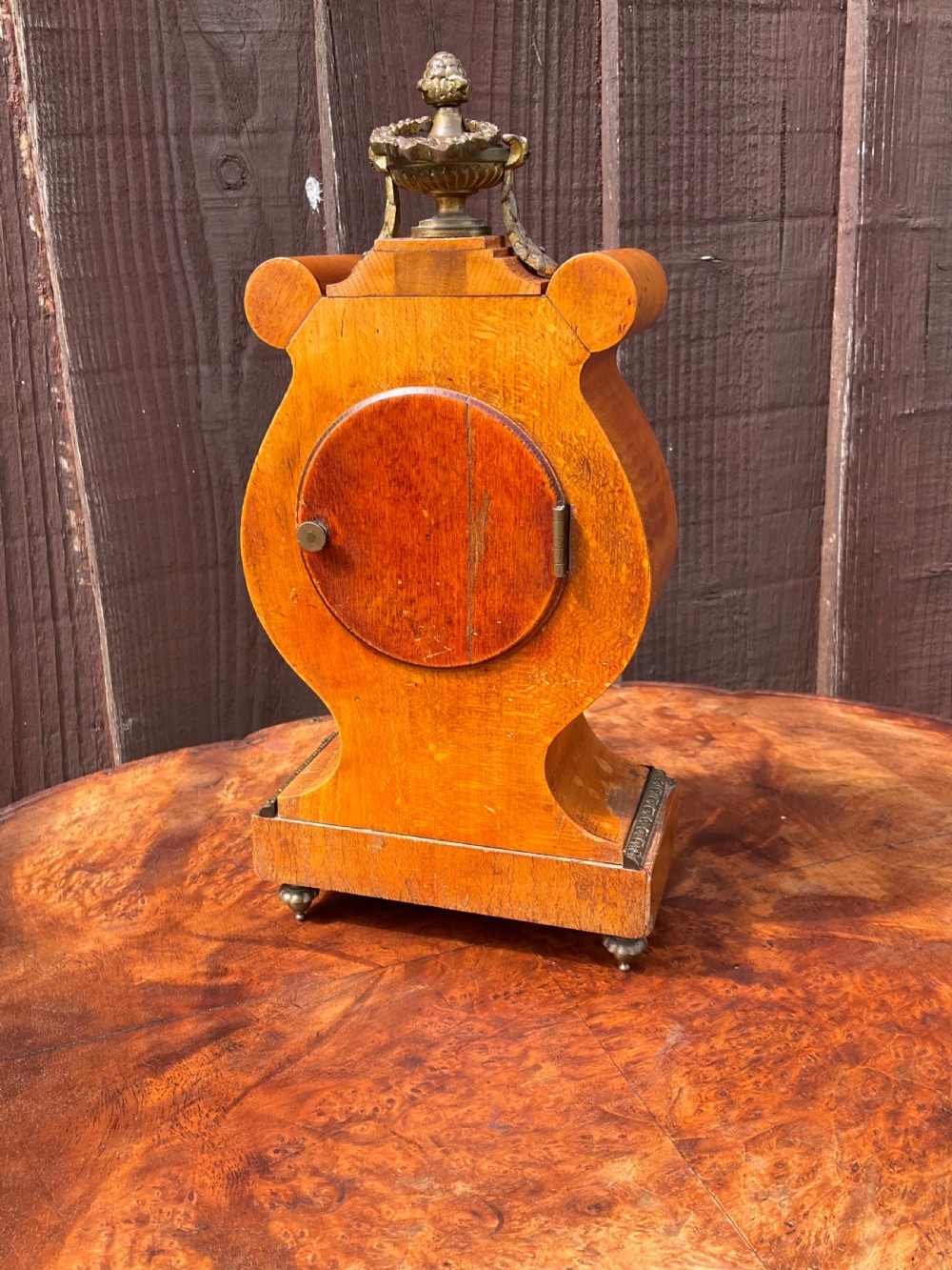 A small lyre-shaped mantel clock featuring figured burr walnut veneer, gilt ormolu swags, an urn finial, and an enamelled dial with Arabic numerals. View IV