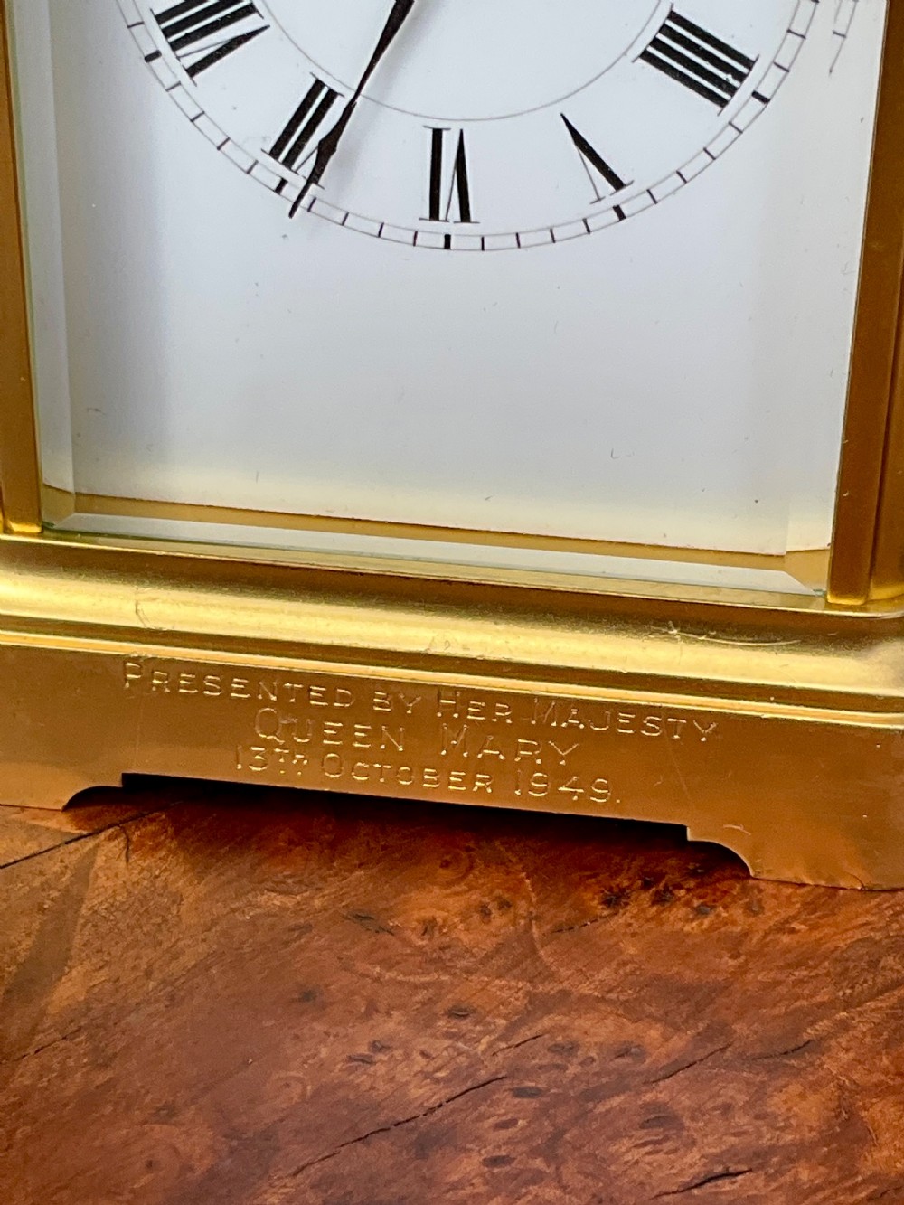 A rectangular gilt brass carriage clock featuring a top carrying handle, a circular top window displaying the balance wheel, and a white dial with Roman numerals. View II