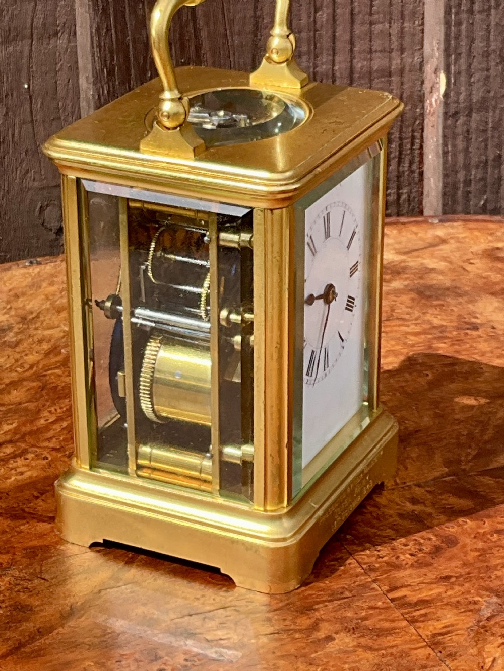 A rectangular gilt brass carriage clock featuring a top carrying handle, a circular top window displaying the balance wheel, and a white dial with Roman numerals. View IX