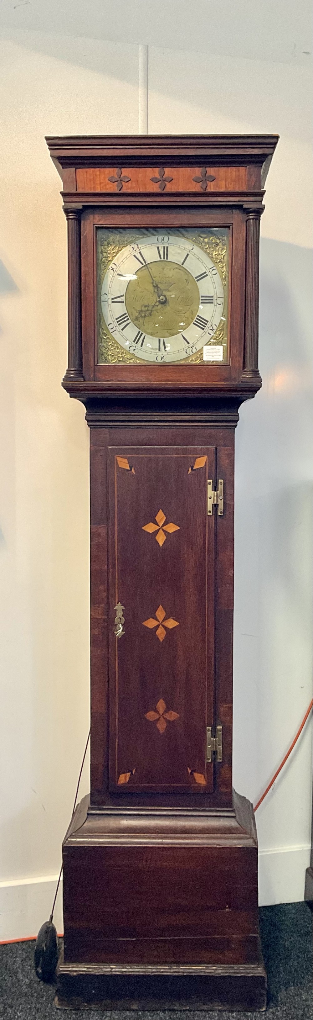A Georgian mahogany longcase clock featuring geometric wood inlay, a brass dial with a silvered chapter ring, and turned columns flanking the hood.