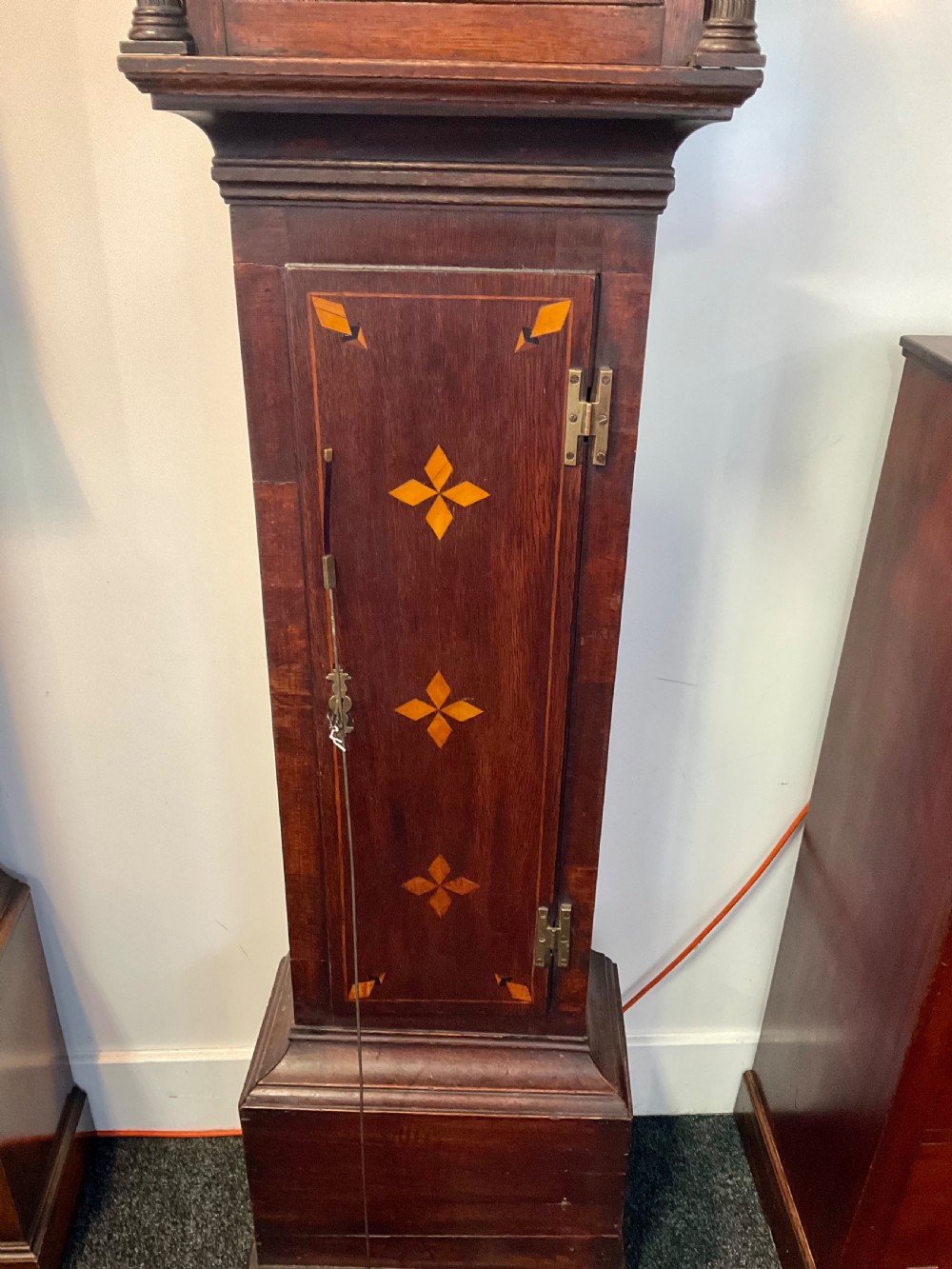 A Georgian mahogany longcase clock featuring geometric wood inlay, a brass dial with a silvered chapter ring, and turned columns flanking the hood. View VII