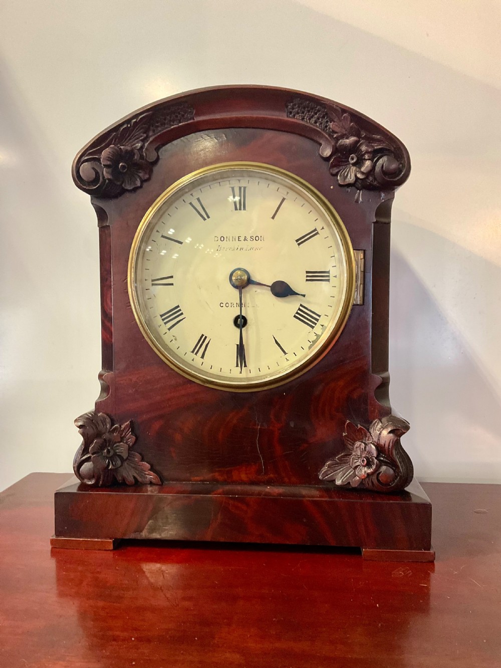 A 19th-century mahogany fusee bracket clock featuring an arched case with hand-carved floral spandrels, flame mahogany veneer, and a circular cream dial with Roman numerals.