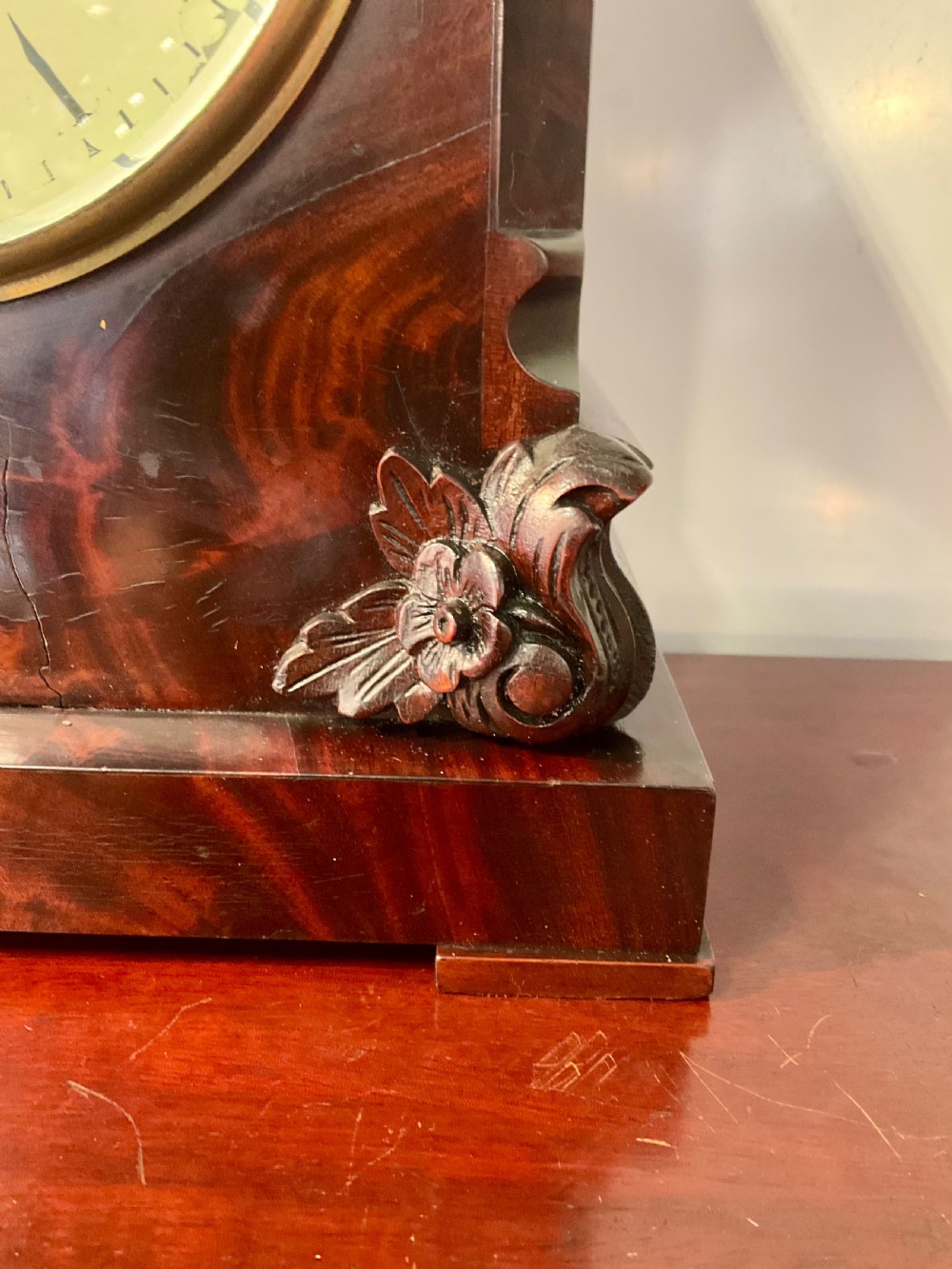 A 19th-century mahogany fusee bracket clock featuring an arched case with hand-carved floral spandrels, flame mahogany veneer, and a circular cream dial with Roman numerals. View VII