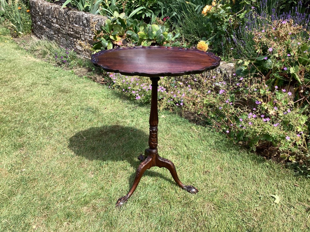 A dark mahogany tripod table featuring a scalloped piecrust tilt-top surface, turned column stem, and carved cabriole legs.
