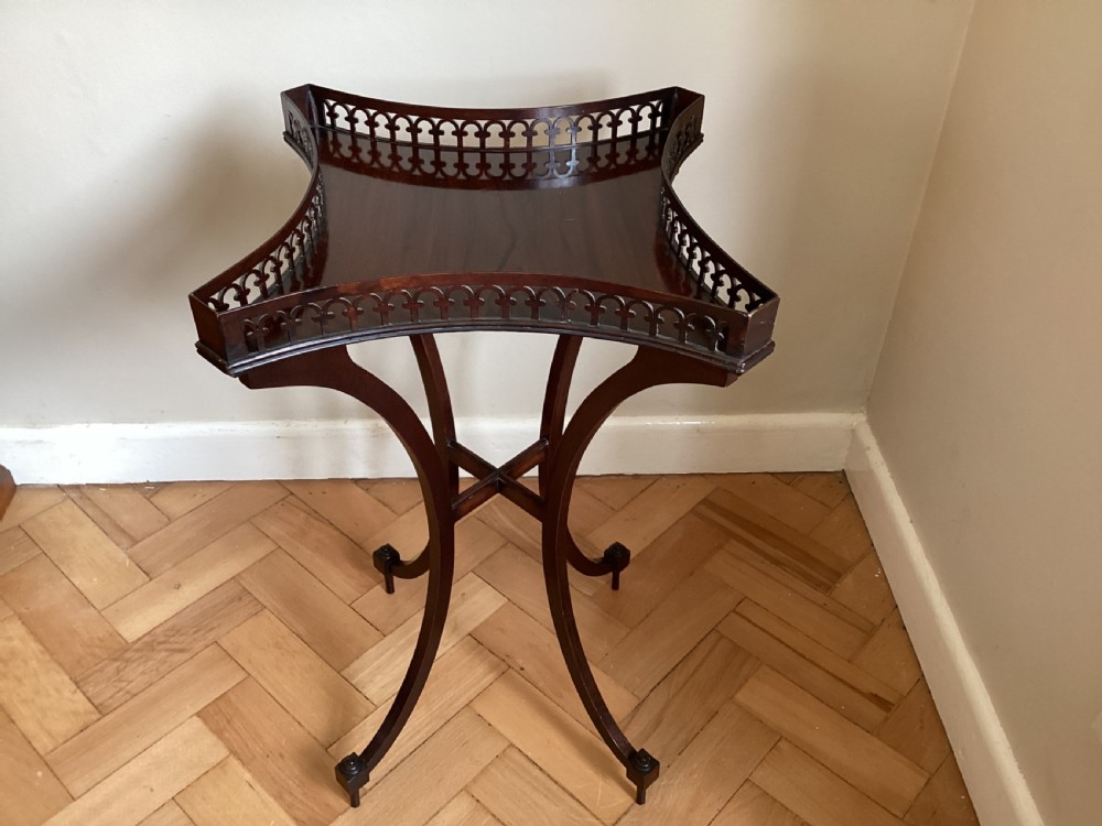 A dark mahogany occasional table featuring a concave square top surrounded by a pierced fretwork gallery, supported by four out-swept legs joined by an X-stretcher.