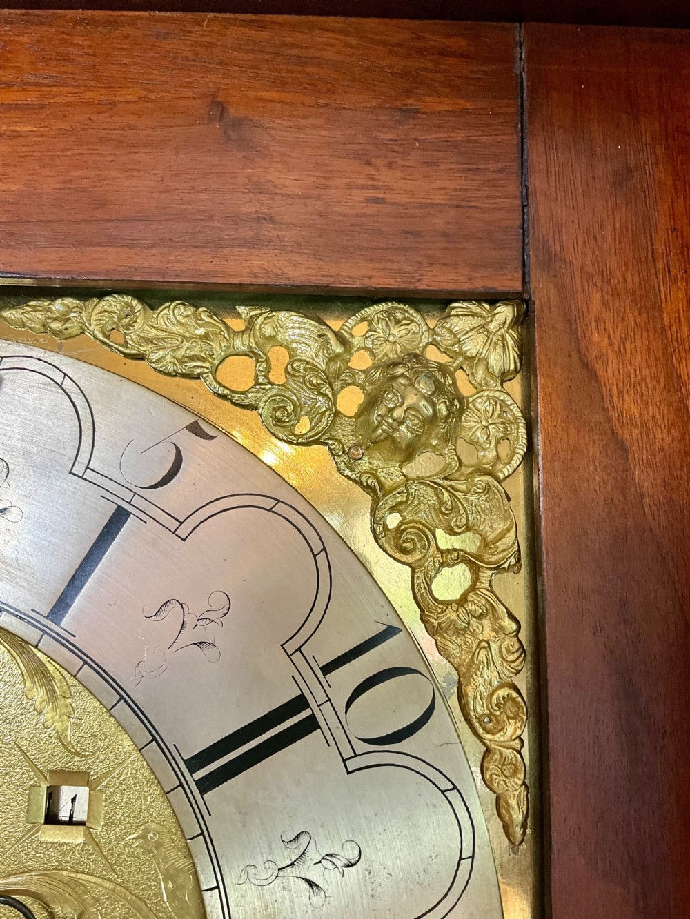 A close-up detail of an antique brass clock dial featuring a hand-painted penny moon face set against a blue sky with gold stars. View XV