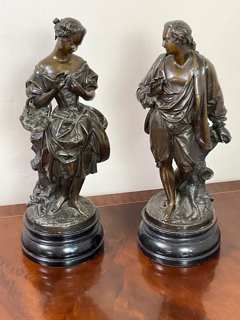 A pair of early 19th-century French patinated bronze figures depicting a man and a woman in period attire on stepped circular bases.