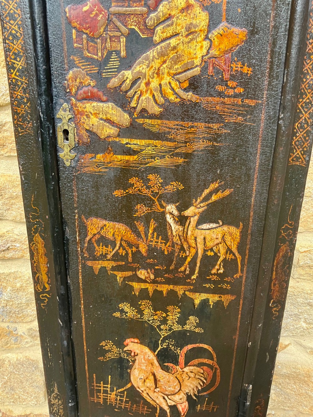 An early Georgian black japanned longcase clock featuring raised gilt Chinoiserie landscapes and figures on the case door, topped with an arched brass dial. View IV
