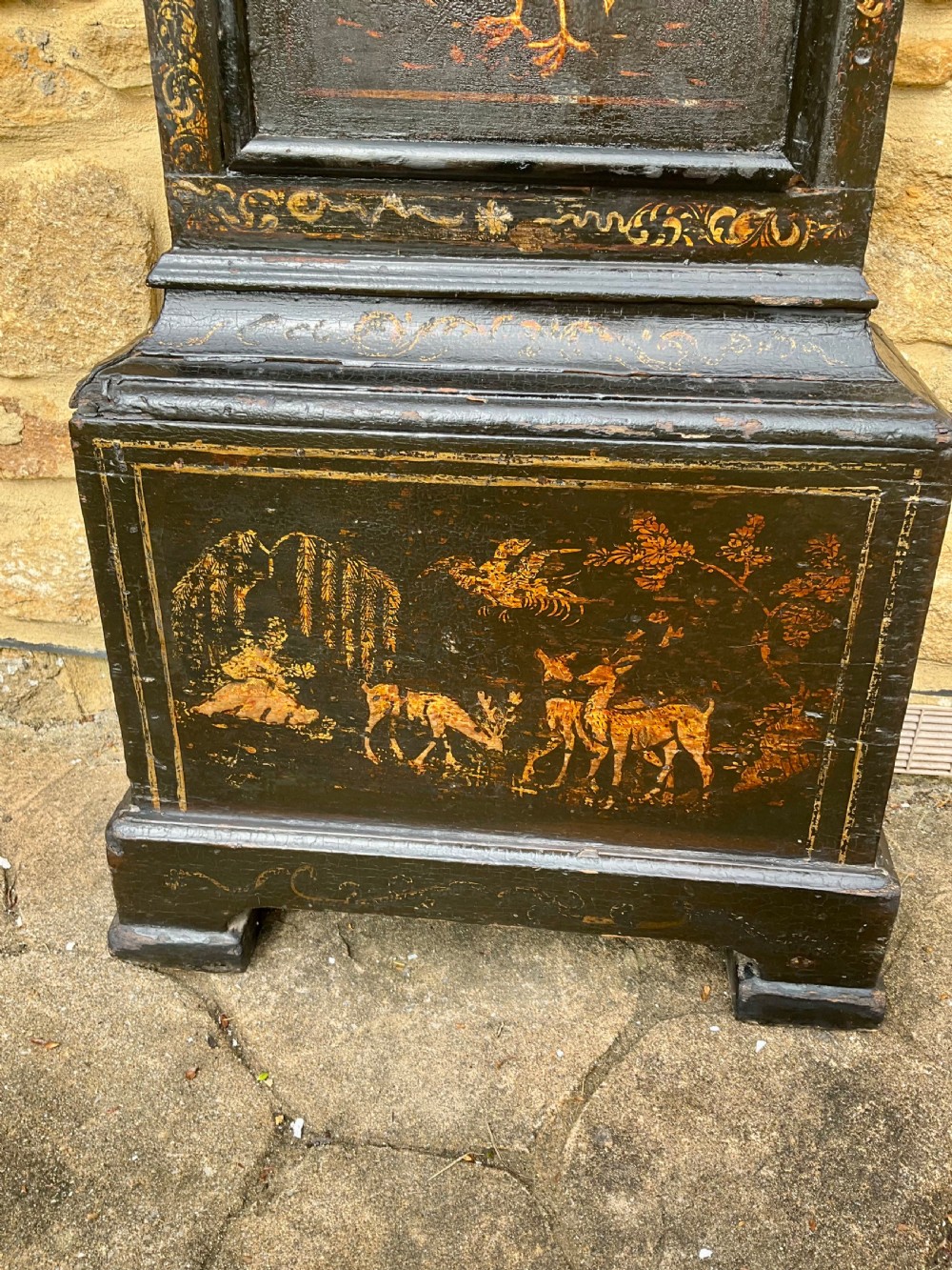 An early Georgian black japanned longcase clock featuring raised gilt Chinoiserie landscapes and figures on the case door, topped with an arched brass dial. View V