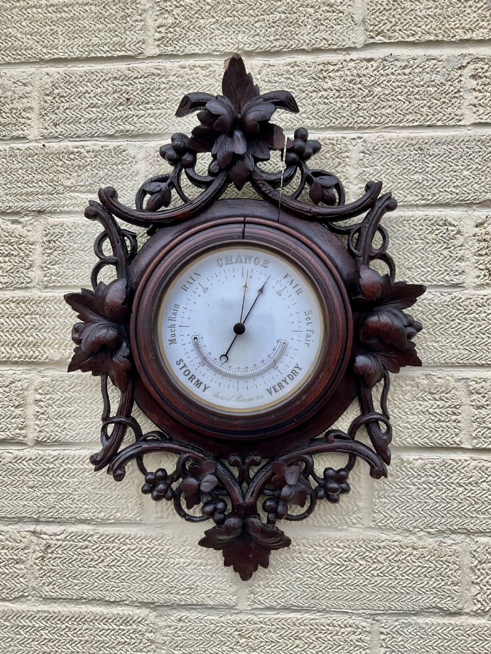 A 19th-century Black Forest aneroid barometer featuring a carved dark wood frame with leaf and acorn motifs surrounding a circular white ceramic dial.