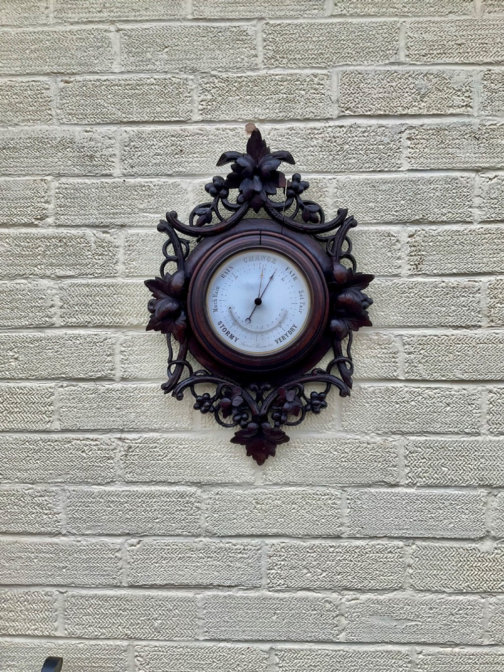 A 19th-century Black Forest aneroid barometer featuring a carved dark wood frame with leaf and acorn motifs surrounding a circular white ceramic dial. View II