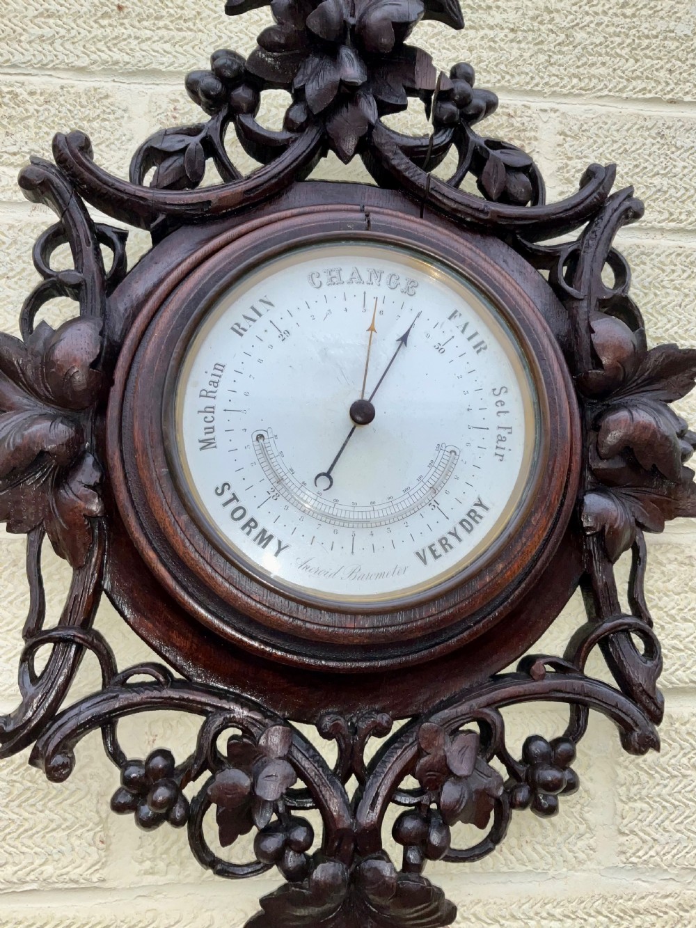 A 19th-century Black Forest aneroid barometer featuring a carved dark wood frame with leaf and acorn motifs surrounding a circular white ceramic dial. View XII