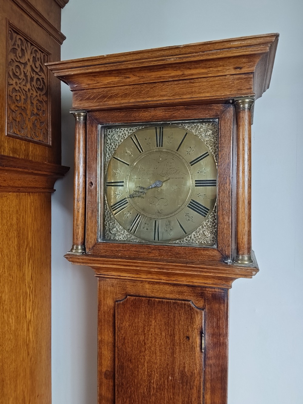 An 18th-century oak longcase clock with an eleven-inch square brass dial, turned hood columns, and a plain wooden trunk door. View XXII