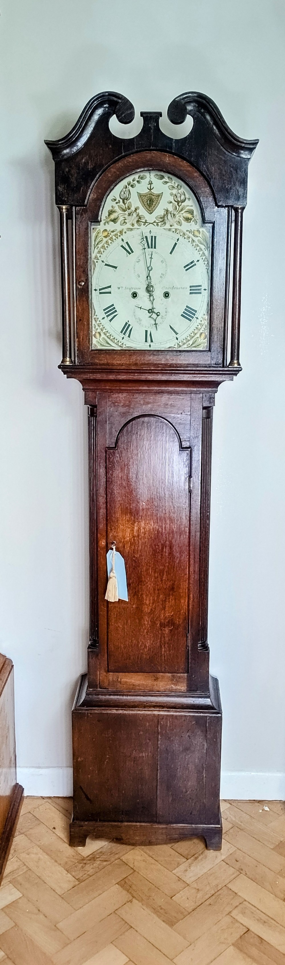 An antique Georgian dark oak grandfather clock featuring a swan-neck pediment, fluted columns, an arched trunk door, and a hand-painted floral dial.