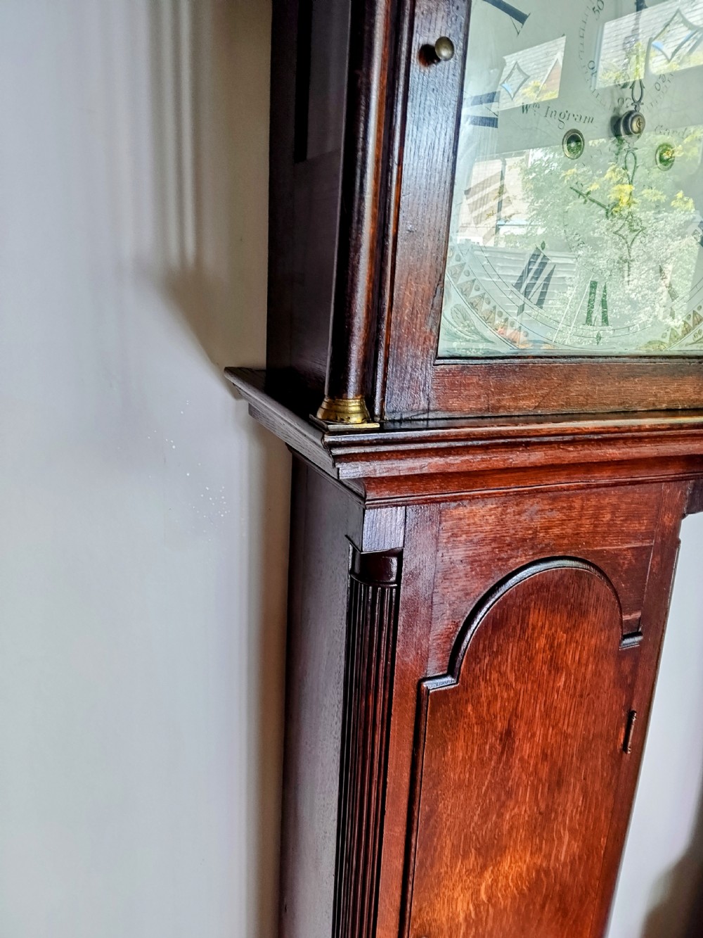 An antique Georgian dark oak grandfather clock featuring a swan-neck pediment, fluted columns, an arched trunk door, and a hand-painted floral dial. View XI