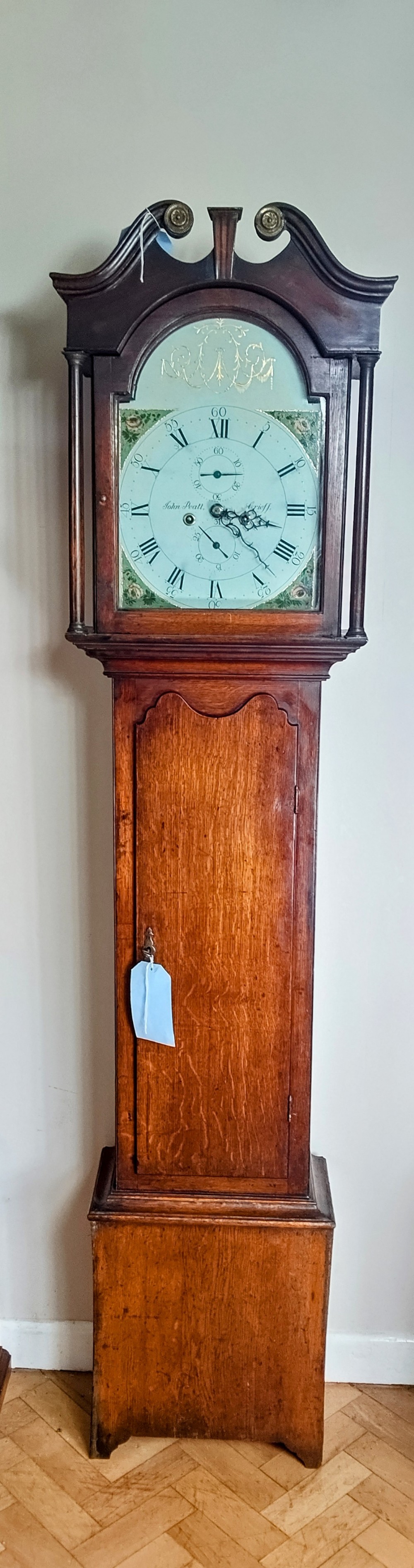 A Georgian oak and mahogany longcase clock featuring a swan-neck pediment, brass patera ornaments, fluted columns, and a painted arch dial.